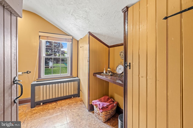 interior space with a textured ceiling, wood walls, radiator heating unit, and vaulted ceiling