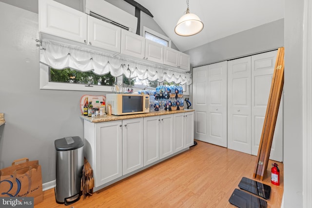 kitchen featuring pendant lighting, vaulted ceiling, white cabinetry, and an AC wall unit