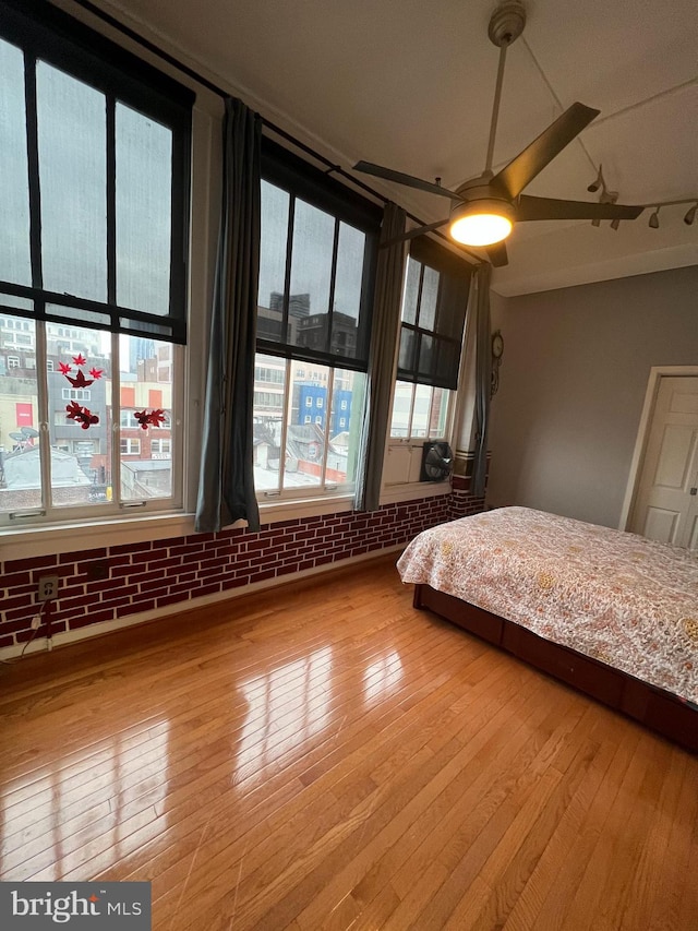 unfurnished bedroom with ceiling fan, hardwood / wood-style flooring, and brick wall