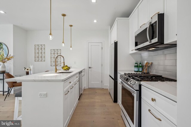 kitchen with light wood-type flooring, appliances with stainless steel finishes, decorative light fixtures, and white cabinets