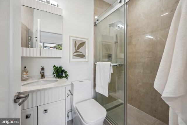 bathroom featuring toilet, vanity, and a shower with shower door