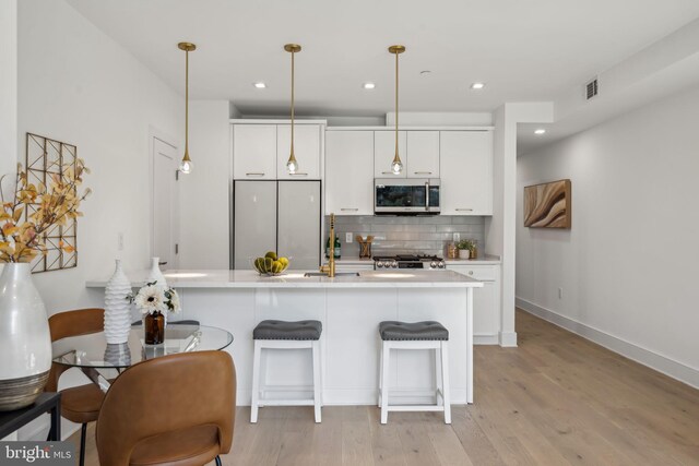 kitchen featuring appliances with stainless steel finishes, decorative light fixtures, white cabinets, a kitchen breakfast bar, and light hardwood / wood-style floors