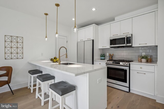 kitchen with stainless steel appliances, hanging light fixtures, sink, and light wood-type flooring