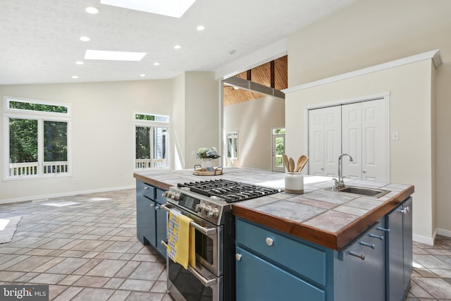 kitchen with tile countertops, a skylight, blue cabinets, double oven range, and a center island with sink