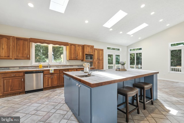 kitchen with appliances with stainless steel finishes, a skylight, a healthy amount of sunlight, a center island with sink, and tile countertops