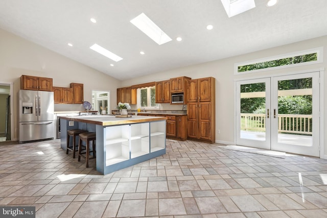 kitchen featuring appliances with stainless steel finishes, a kitchen island with sink, a skylight, a kitchen bar, and french doors