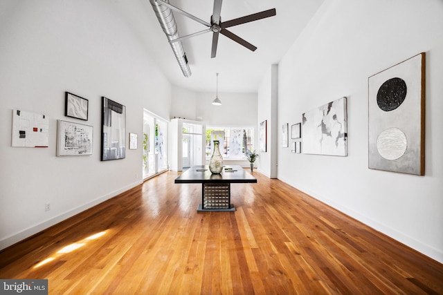 unfurnished living room with wood-type flooring, ceiling fan, and a towering ceiling