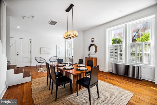 dining space featuring a notable chandelier, radiator, and hardwood / wood-style flooring