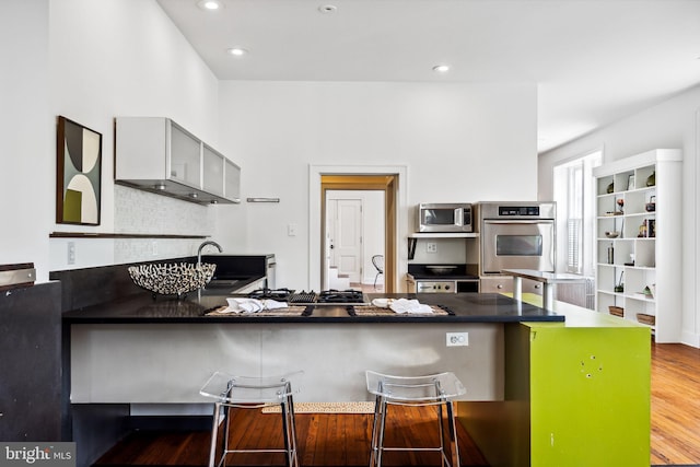 kitchen with kitchen peninsula, gray cabinets, a breakfast bar area, hardwood / wood-style flooring, and sink