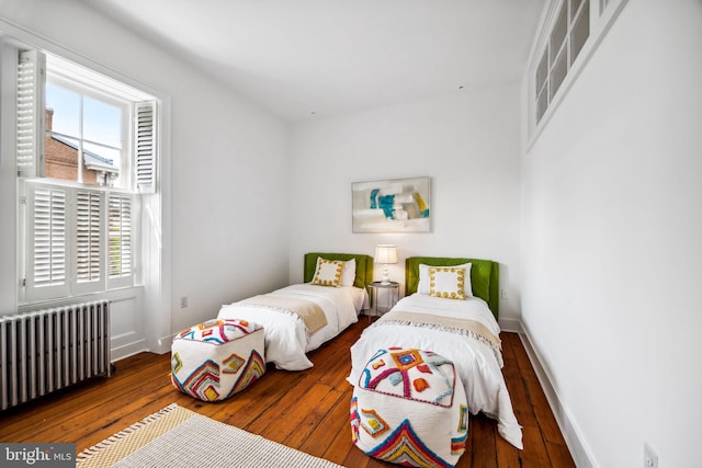 bedroom with wood-type flooring, radiator heating unit, and multiple windows