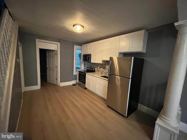 kitchen featuring white cabinets, backsplash, light wood-type flooring, stainless steel appliances, and ornate columns