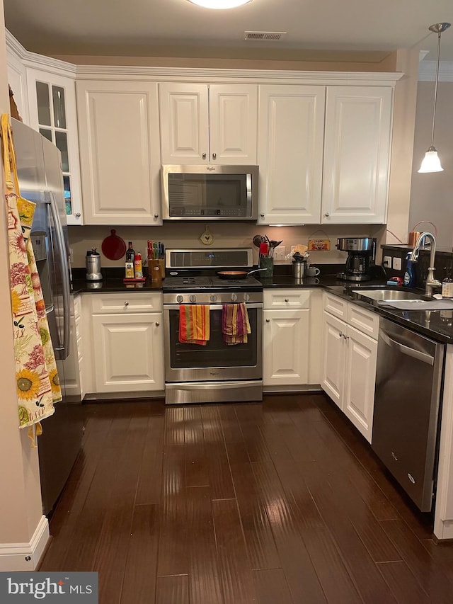 kitchen with appliances with stainless steel finishes, sink, pendant lighting, dark hardwood / wood-style floors, and white cabinetry