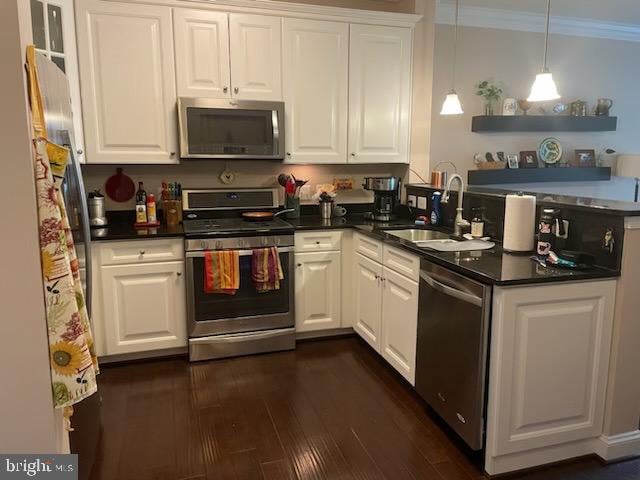 kitchen with pendant lighting, dark wood-type flooring, crown molding, white cabinetry, and stainless steel appliances