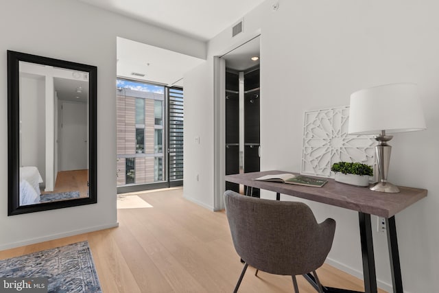 home office with a wall of windows and light hardwood / wood-style flooring