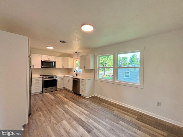 kitchen with white cabinetry, sink, hanging light fixtures, stainless steel appliances, and light hardwood / wood-style flooring