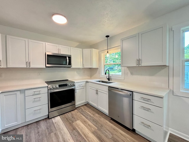 kitchen featuring white cabinets, appliances with stainless steel finishes, pendant lighting, and sink