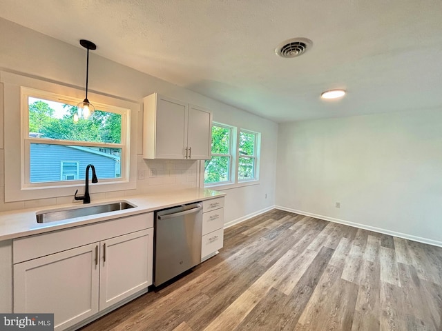 kitchen featuring stainless steel dishwasher, sink, light hardwood / wood-style floors, white cabinetry, and hanging light fixtures