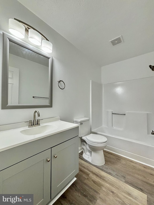 full bathroom featuring vanity, a textured ceiling, shower / tub combination, hardwood / wood-style flooring, and toilet