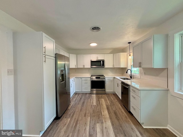 kitchen with light wood-type flooring, stainless steel appliances, sink, pendant lighting, and white cabinetry