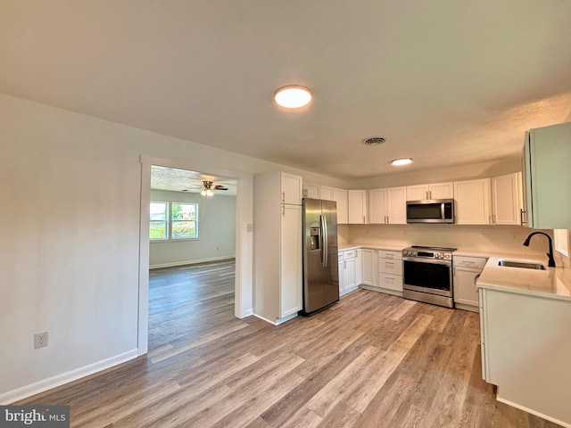 kitchen with sink, white cabinets, light wood-type flooring, and appliances with stainless steel finishes