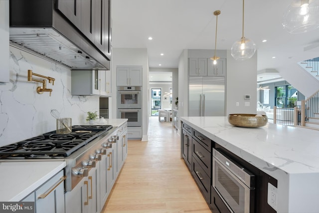 kitchen featuring exhaust hood, hanging light fixtures, built in appliances, decorative backsplash, and light hardwood / wood-style floors