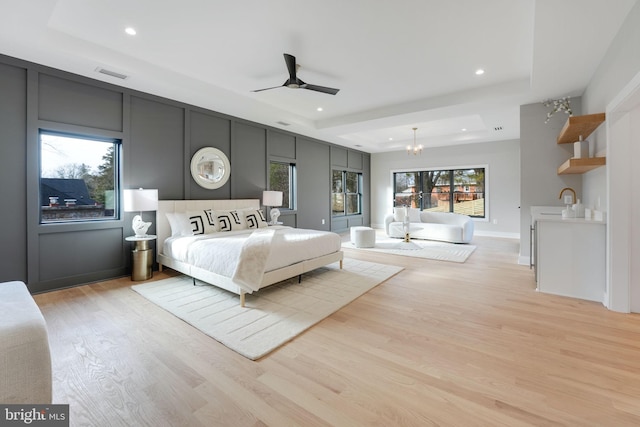 unfurnished bedroom featuring ceiling fan with notable chandelier, light hardwood / wood-style floors, and a tray ceiling