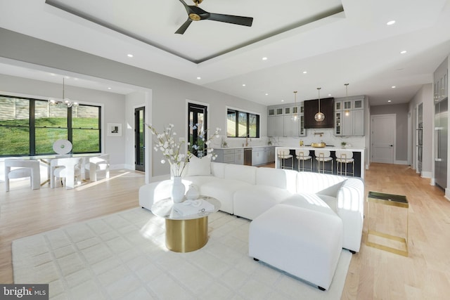 living room with a tray ceiling, light hardwood / wood-style flooring, and ceiling fan with notable chandelier