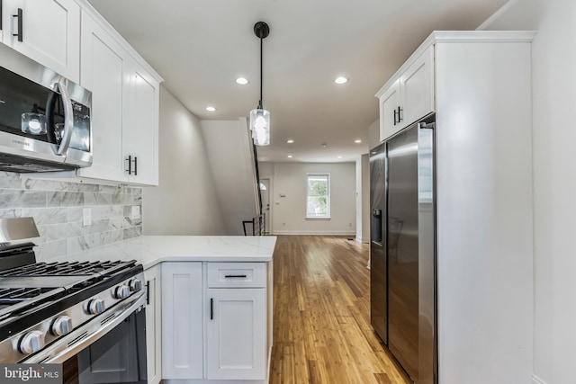 kitchen with white cabinets, appliances with stainless steel finishes, backsplash, and light hardwood / wood-style flooring