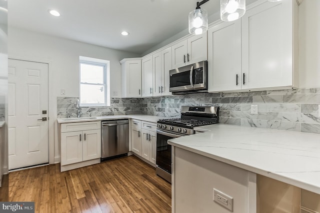 kitchen with appliances with stainless steel finishes, dark wood-type flooring, white cabinets, and decorative light fixtures