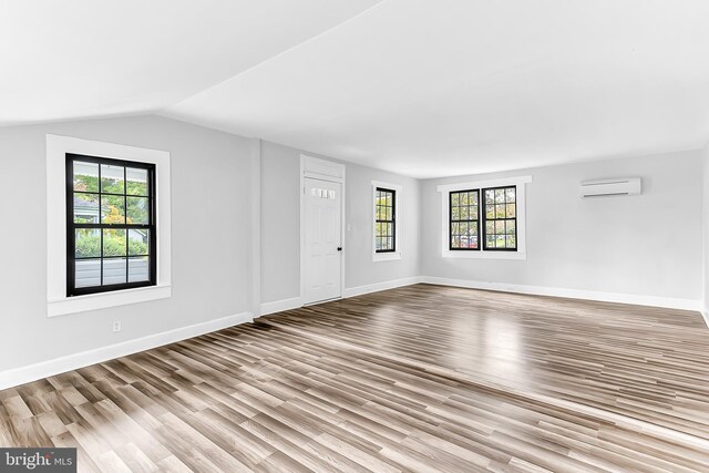 spare room with light wood finished floors, baseboards, vaulted ceiling, and a wall mounted air conditioner