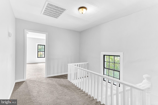 corridor featuring carpet, visible vents, baseboards, and an upstairs landing