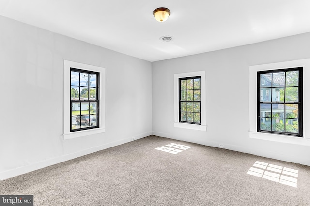 carpeted spare room with a wealth of natural light, visible vents, and baseboards