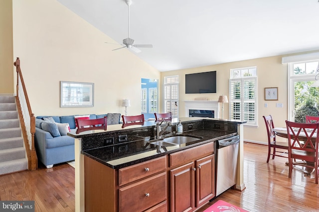 kitchen with dishwasher, a high end fireplace, dark stone countertops, hardwood / wood-style floors, and sink