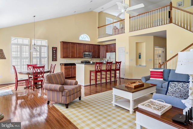 living room with ceiling fan with notable chandelier, high vaulted ceiling, and light wood-type flooring