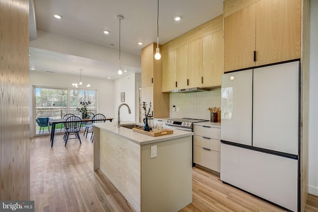 kitchen with decorative light fixtures, light hardwood / wood-style flooring, backsplash, white fridge, and a center island with sink