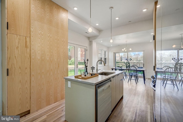 kitchen with light hardwood / wood-style flooring, sink, stainless steel dishwasher, hanging light fixtures, and an island with sink