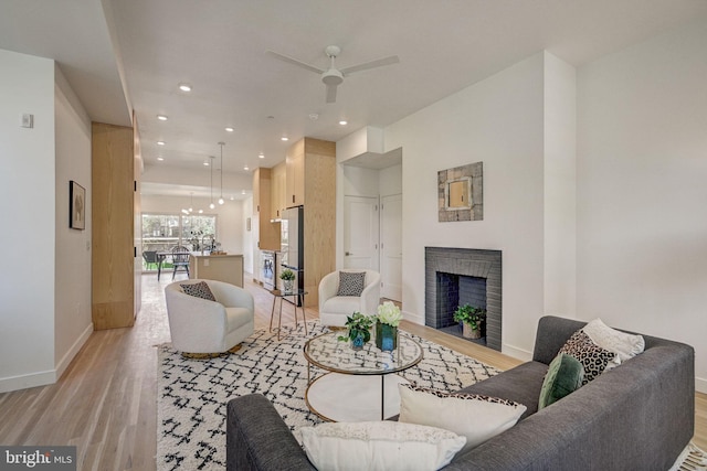 living room featuring a fireplace, ceiling fan, and light wood-type flooring