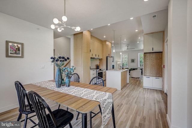 dining space featuring ceiling fan with notable chandelier, sink, and light hardwood / wood-style floors