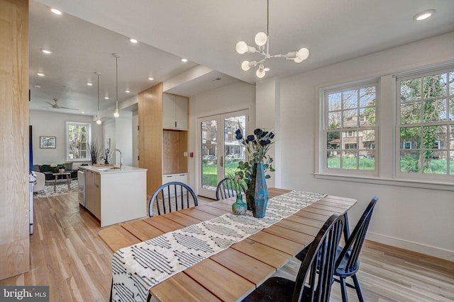 dining space featuring ceiling fan with notable chandelier, sink, and light wood-type flooring