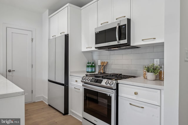 kitchen with white cabinets, decorative backsplash, stainless steel appliances, light stone countertops, and light wood-type flooring