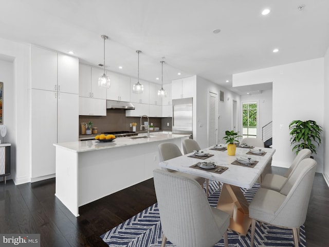 kitchen featuring stainless steel appliances, dark wood-type flooring, sink, white cabinets, and an island with sink