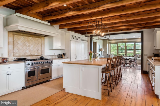 kitchen with white cabinets, custom exhaust hood, range with two ovens, and an island with sink