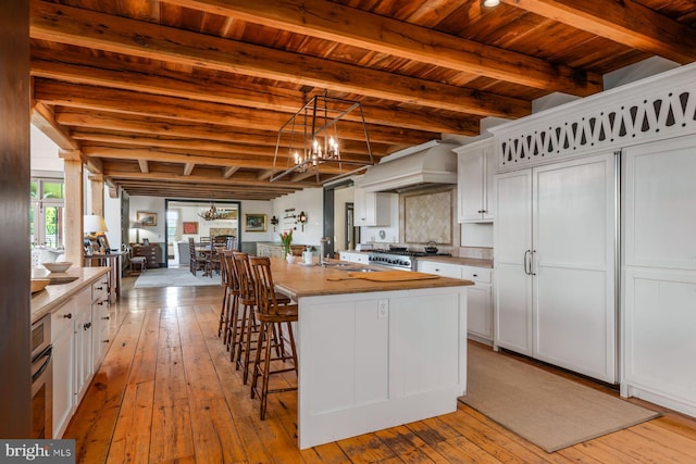 kitchen with a center island with sink, white cabinets, wood ceiling, and custom range hood