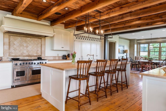 kitchen featuring white cabinets, pendant lighting, range with two ovens, and an island with sink