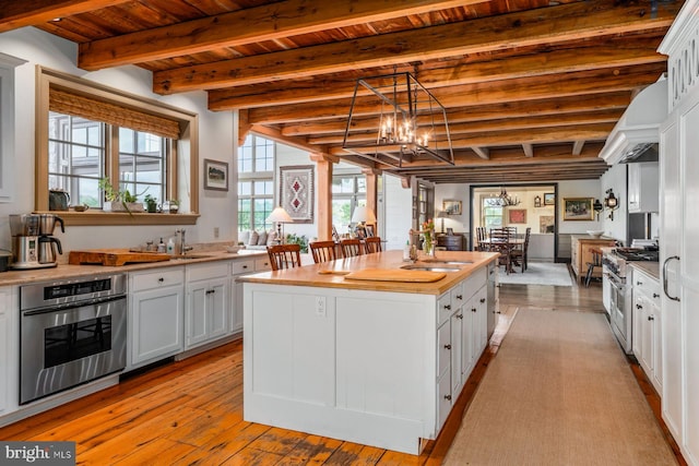 kitchen with stainless steel appliances, sink, beam ceiling, a center island, and white cabinetry