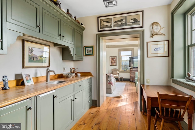 bar featuring butcher block countertops, green cabinets, sink, and light wood-type flooring