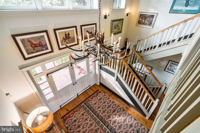 stairway featuring hardwood / wood-style flooring, a healthy amount of sunlight, a towering ceiling, and an inviting chandelier