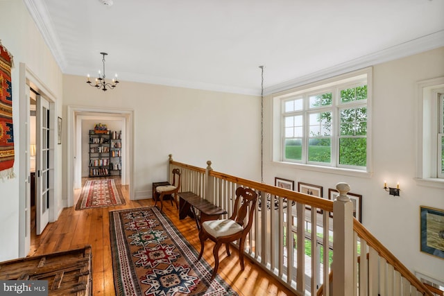 hallway with crown molding, wood-type flooring, and an inviting chandelier