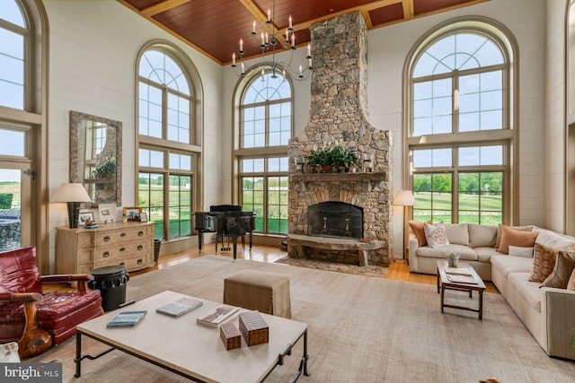 living room featuring a towering ceiling, light hardwood / wood-style floors, a stone fireplace, and wooden ceiling