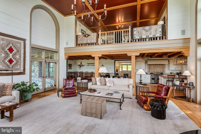 living room with french doors, a towering ceiling, wood ceiling, wood-type flooring, and an inviting chandelier